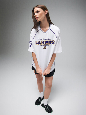 Modelka v bílé košili Los Angeles Lakers a černých šortkách na šedém pozadí.
