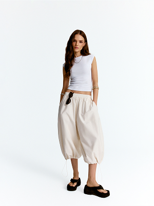 Modelka v bílém topu a širokých 3/4 kalhotách.